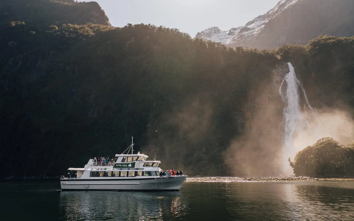 A cruise boat beside a waterfall on the walls of Milford Sound