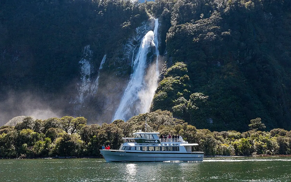 A cruise boat beside a waterfall in Milford Sound