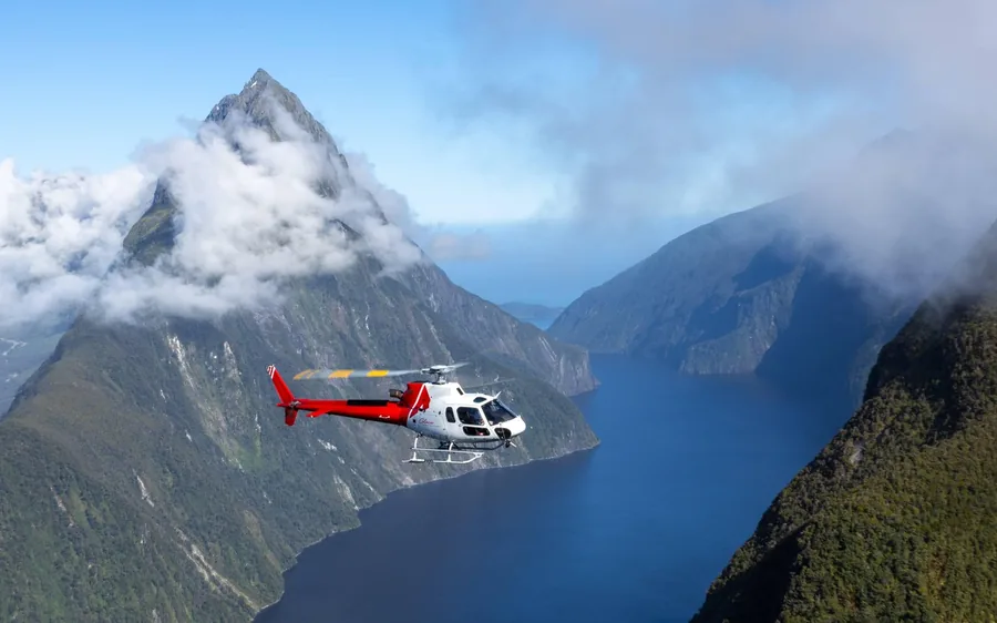 A helicopter flying over Milford Sound with Mitre Peak behind